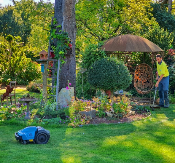 Salarié qui entretient un jardin avec une débroussailleuse et un robot tondeuse
